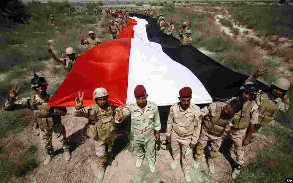 Iraqi military cadets hold a large version of their national flag as they flash the victory sign during their graduation ceremony in the Jurf al-Sakher area, some 50 kilometres south of Baghdad, on April 9. (AFP/Haidar Hamdani)