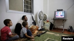 A Free Syrian Army fighter watches US President Barack Obama's speech with his family in Ghouta, Damascus, August 31, 2013