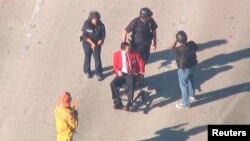Полицейские сопровождают пострадавшего во время стрельбы в аэропорту мужчину к машине скорой помощи. Лос-Анджелес, 1 ноября 2013 года.