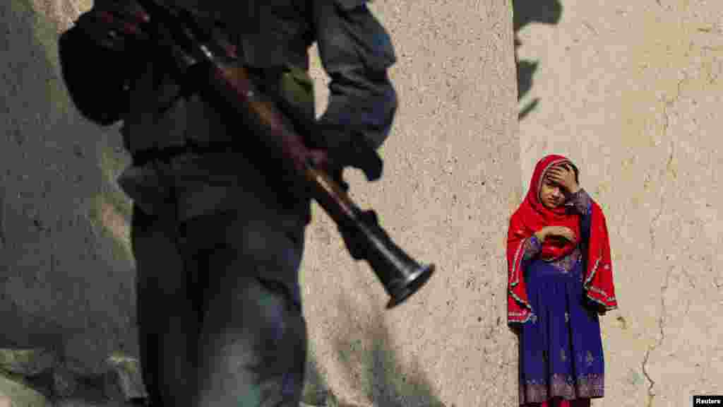 A girl watches as a member of the Afghan security forces walks by near the town of Ahmad Khel in Paktiya Province on July 16. (REUTERS/Lucas Jackson)