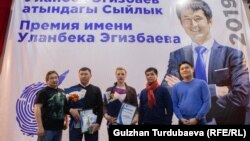 Kyrgyzstan - RFE/RL investigative journalist Ydyrys Isakov (second from left) won the top prize in the Investigative Journalism Foundation in Kyrgyzstan’s annual prize dedicated to late RFE/RL colleague Ulanbek Egizbayev, whose image is displayed on the banner in the background.
