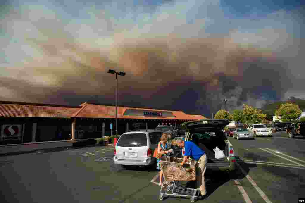 Shoppers load groceries as smoke from a forest fire billows over Clearlake, California. The fire, one of dozens raging in drought-parched northern California, has destroyed dozens of homes and scorched 22,000 hectares. (epa/Noah Berger)