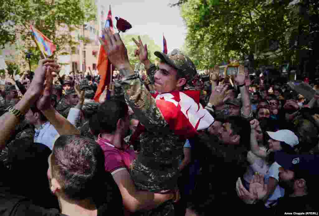 A soldier who has joined protests in Yerevan is carried above the crowd after being given a red rose.