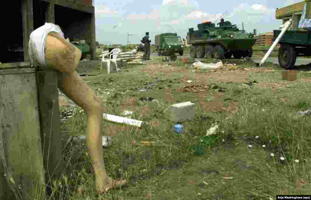 Parts of a plastic mannequin stand next to a destroyed house on the outskirts of Glogovac, 35 kilometers west of Pristina, on June 17, 1999, while NATO vehicles drive through the area.