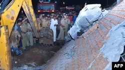 Indian officials and bystanders gather beside a collapsed building after an explosion and fire at a temple in Paravoor early on April 10 that killed scores of people. 