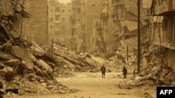 Syrians walk amid debris during a sandstorm in the once rebel-held Kastal al-Harami neighborhood in the northern city of Aleppo on March 10.