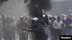 Egypt -- A riot policeman aims a shotgun with rubber bullets at protesters, next to a plainclothes policeman during clashes in a side street near Tahrir Square in Cairo, 21Nov2011