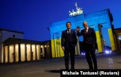 French President Emmanuel Macron (left) and German Chancellor Olaf Scholz visit the Brandenburg Gate while it is illuminated in the colors of the Ukrainian flag, in Berlin on May 9, 2022.