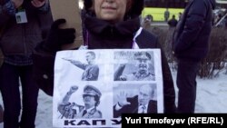 A woman holds a sign featuring Adolf Hitler, Josef Stalin, Muammar Qaddafi, and Vladimir Putin, and below it says "Kaput!"