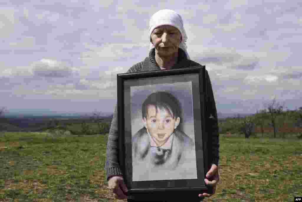 Sabrije Deliu, a Kosovar woman, poses with a painting depicting her 6-year-old son, Bleart Deliu, who was killed during the Kosovo War in 1999, during a ceremony marking the 18th anniversary of the massacre in the village of Rezalle on April 5. (AFP/Armend Nimani)