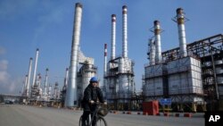 FILE - In this Dec. 22, 2014 file photo, an Iranian oil worker rides his bicycle at the Tehran oil refinery