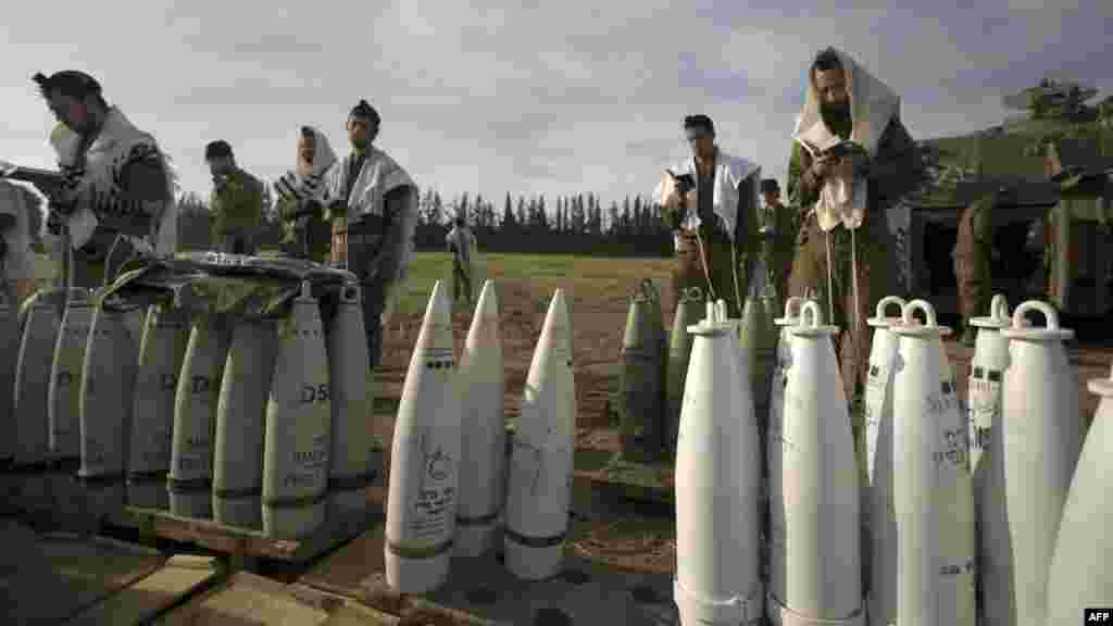 Israeli soldiers perform morning prayers next to artillery shells at an Israeli Army deployment area near the Israel-Gaza Strip border. (AFP/Menahem Kahana)