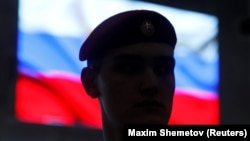 Военный на фоне изображения российского флага на экране.
