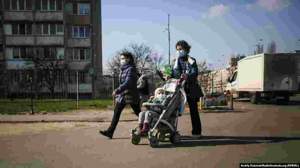 Женщины с ребенком в медицинских масках идут по улице возле метро &quot;Героев Дпепра&quot;. Карантин в Украине продлится минимум до 3 апреля 2020 года