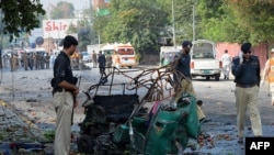 Police officials stand beside a mangled auto-rickshaw at the site of a suicide bomb attack in Peshawar, September 23, 2014.