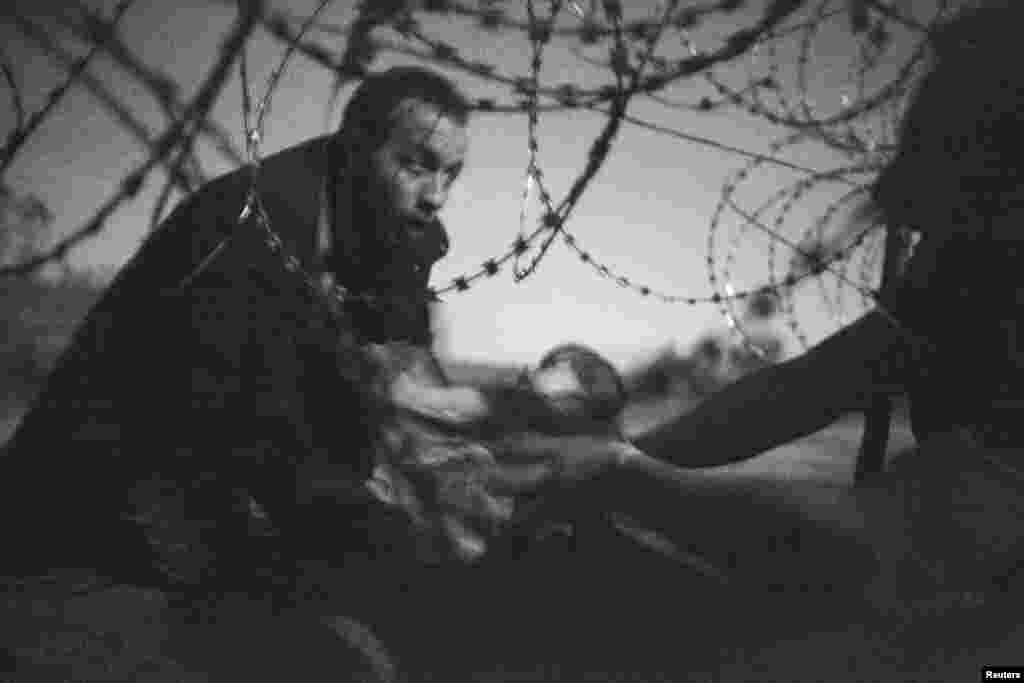 World Press Photo of the Year 2015 and Spot News 1st Prize Singles was won by freelance photographer Warren Richardson for this image. The photo, taken in near darkness, depicts a migrant passing a baby under the fence at the Serbia/Hungary border in Roszke, Hungary. (August 28, 2015)