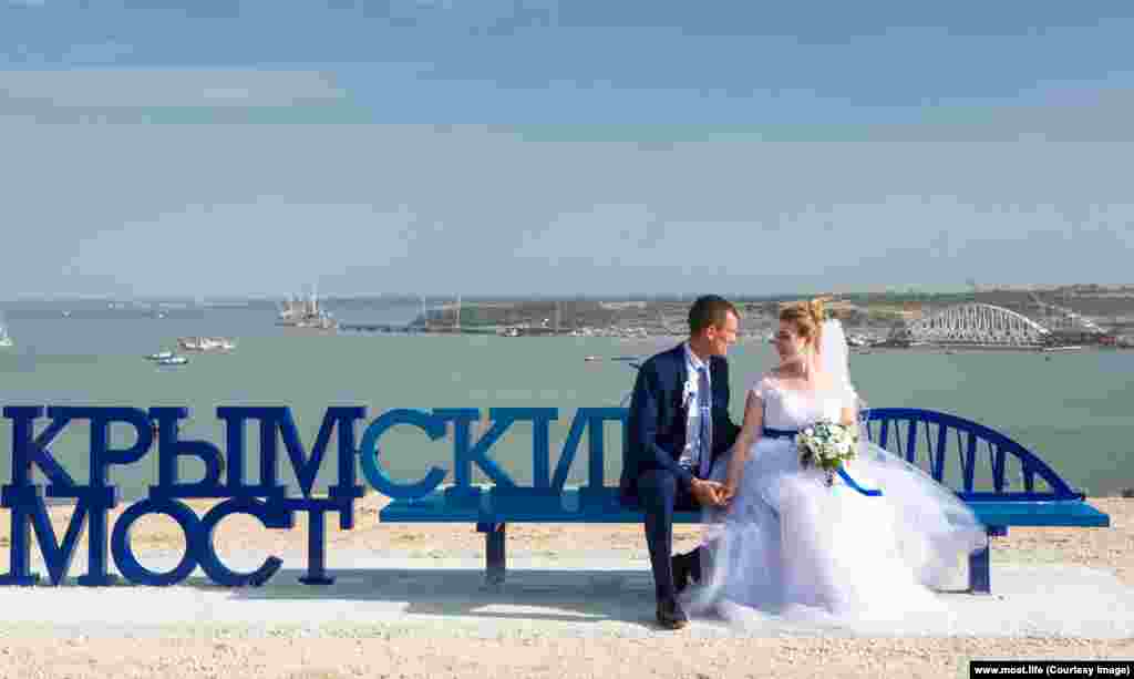 Newlyweds perch on a freshly installed bench overlooking the Crimean end of the bridge.