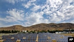 In this June, 22, 2014 photo, a man looks at solar panels at the Taleghan Renewable Energy Site in Taleghan, 160 kilometers (99 miles) northwest of capital Tehran, Iran. President Hassan Rouhani’s government has quintupled its spending on solar power proj