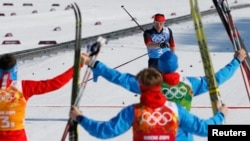 Russia's Maksim Vylegzhanin (top) as he crossed the finish line and was greeted by teammates at the Sochi 2014 Winter Olympic Games