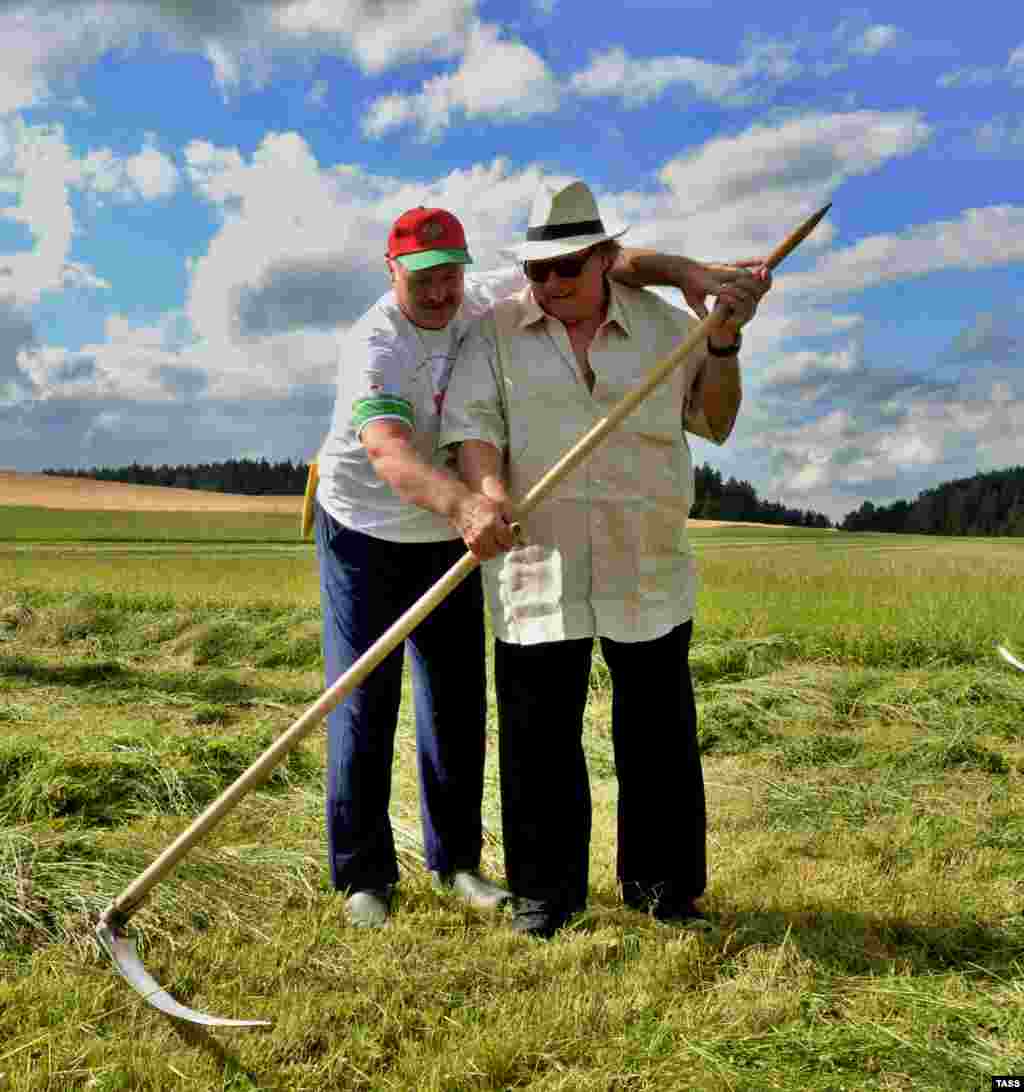 Belarusian President Alyaksandr Lukashenka (left) gives French actor Gerard Depardieu a lesson in how to use a scythe at his official residence outside Minsk. (TASS/BelTA/Andrei Stasevich)