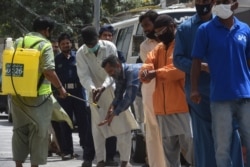 A worker sprays sanitizer on the hands of a man lining up to buy groceries from a government-subsidized store during a lockdown in Karachi.