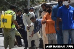 A worker sprays sanitizer on the hands of a man lining up to buy groceries from a government-subsidized store during a lockdown in Karachi.