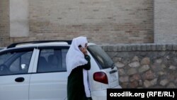 Uzbekistan - an Uzbek woman talking on a mobile passing from Uzbek car Matiz, undated