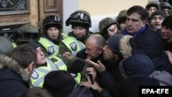 Міхеїл Саакашвілі (праворуч) спостерігає, як мітингувальники, яких він закликав йти до Жовтневого палацу, під час штурму будівлі виривають бійця Нацгвардії зі строю перед центральним входом до будівлі. Київ, 17 грудня 2017 року (ілюстраційне фото)