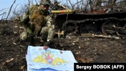 Український військовослужбовець показує фотографу російський документ біля спаленого танка поблизу села Мала Рогань на схід від Харкова, 1 квітня 2022 року