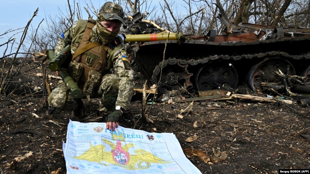 Украинский военнослужащий показывает фотографу российскую стенгазету рядом со сожженным российским танком возле села Мала Рогань к востоку от Харькова, 1 апреля 2022 года