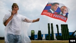 A man holds a flag with portraits of Russian President Vladimir Putin and Prime Minister Dmitry Medvedev in front of S-300 surface-to-air missile systems during a military exhibition outside Moscow in 2014.