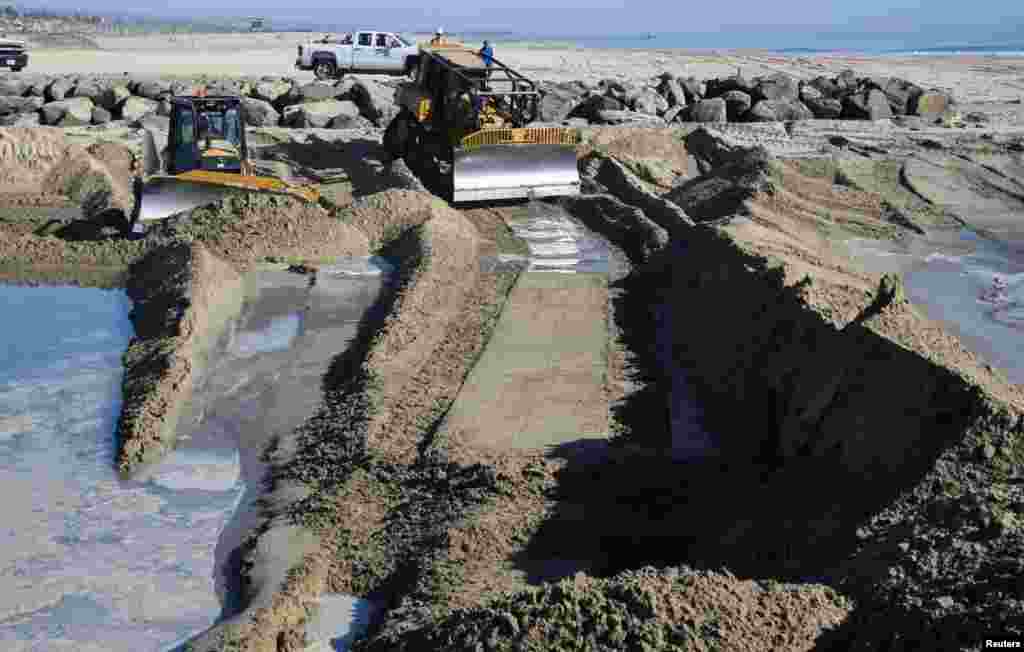 Munkagépekkel homokperemet építenek, hogy megakadályozzák az olaj haladását