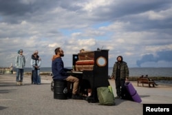 A street musician gives an impromptu concert on the beach in Odesa as smoke rises over the port of Pivdenniy in the distance on April 19.