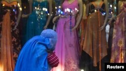 Женщина в бурке проходит мимо витрины магазина женской одежды.