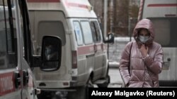 A woman wearing a protective face mask walks past ambulances outside a hospital in Omsk. 