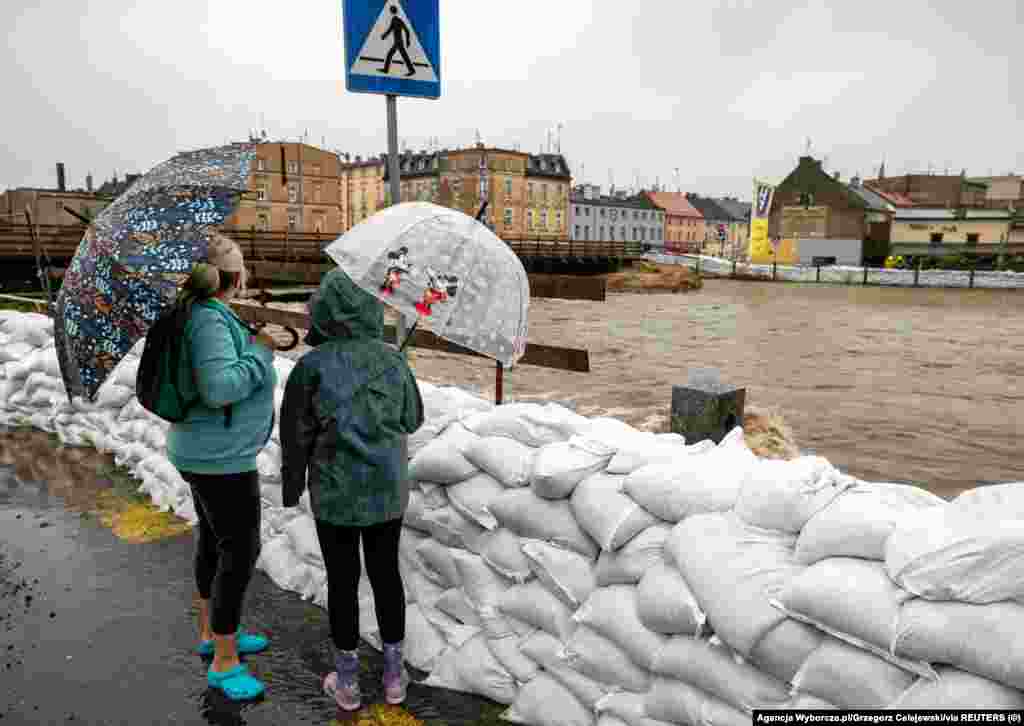 Ljudi sa kišobranima pored vreća pijeska naslaganih na obali rijeke Bialke u Glucholazyju, Poljska, 14. septembra 2024.