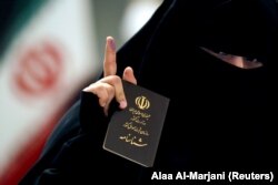 O femeie din Iran care a votat își arată pașaportul și degetul pătat cu cerneală. Cerneala temporară are rolul de a preveni frauda electorală.