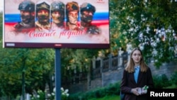 Polina Lermant, în vârstă de 24 de ani, candidată din partea partidului liberal rus Iabloko, împărțind fluturași lângă un ecran cu o ilustrație militară patriotică, înainte ca partidul ei să fie scos din cursa electorală.
