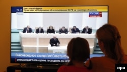 A woman and her daughter watch television during a discussion on the proposal of Russian President Vladimir Putin and the use of Russian armed forces in Ukraine in parliament in Moscow on March 1.