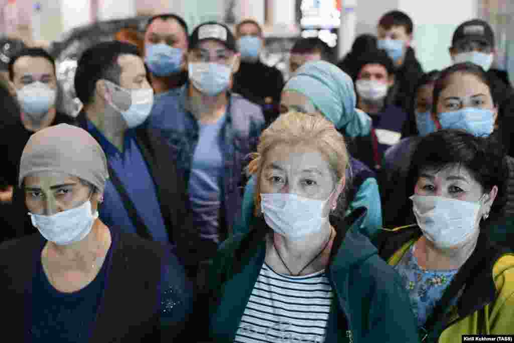 Workers from Kyrgyzstan wear face masks on March 30 as they wait to find out how the can leave Tolmachevo International Airport in Novosibirsk. They do not appear to be practicing physical distancing to prevent the spread of the coronavirus.