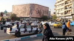 Një poster në sheshin Enqelab në nëntor 2025 kombinon figura historike dhe një incident të vitit 2016 ku ekuipazhet amerikane të flotës u kapën nga forcat iraniane pas një gabimi navigimi. Teksti në farsi thotë: “Do të gjunjëzoheni para Iranit përsëri”.