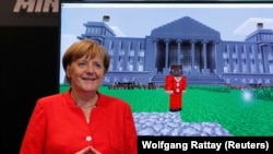 GERMANY -- German Chancellor Angela Merkel stands next to a screen depicting a Minecraft rendition of her and the Reichstag building during the opening of the world's largest computer games fair Gamescom in Cologne, Germany, August 22, 2017. 