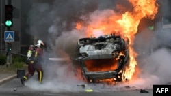 Пожарникар гасне запален автомобил во париското предградие Нантер, 29 јуни 2023 година.