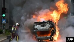Një zjarrfikës duke tentuar të shuajë zjarrin e një makine të djegur në Nanterre. 29 qershor 2023.