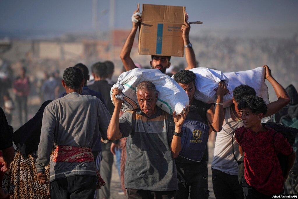 Burra e fëmijë palestinezë duke bartur thasë dhe pako me ndihma.