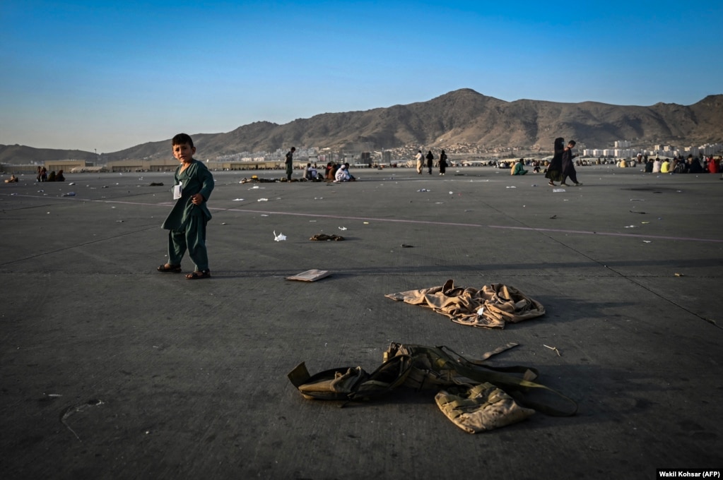 Një fëmijë afgan, duke ecur pranë uniformave ushtarake, teksa bashkë me familjen e tij priste të largohej nga aeroporti i Kabulit, pas kthimit të talibanëve në pushtet, në Afganistan, më 16 gusht.