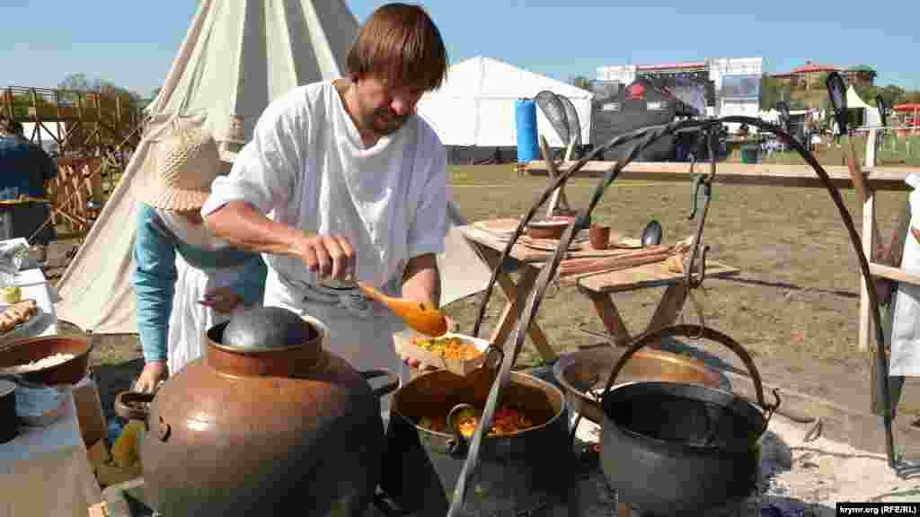 Реконструктор подает средневековое генуэзское блюдо в картонной коробочке на празднике виноделия в Балаклаве