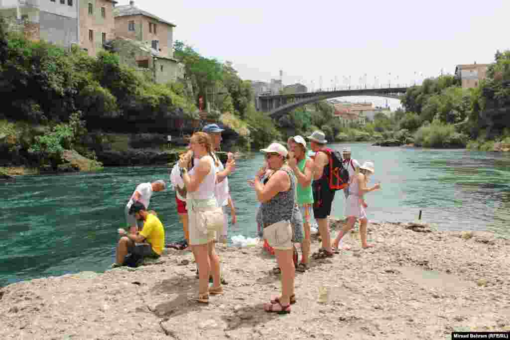 Grupa turista iz Poljske na obali Neretve ispod Starog mosta u Mostaru jedu sladolede, pokušavajući se rashladiti usred velike vrućine iza 13 sati.