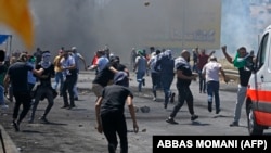 Палестинские демонстранты бросают камни в сторону израильских сил безопасности во время столкновений на Западном берегу. 14 мая 2021 года.