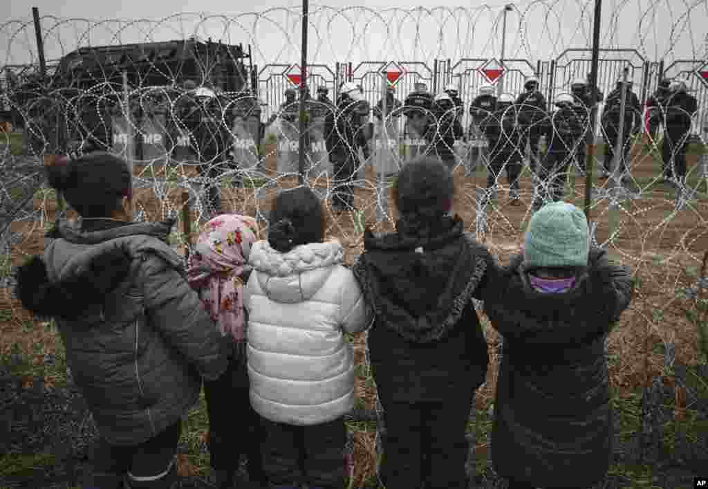 Mai mulți copii stau în fața unui gard de sârmă ghimpată păzit de militari polonezi, la punctul de control Kuznița, de la granița belarusă-polonă, lângă Hrodna, Belarus.&nbsp;